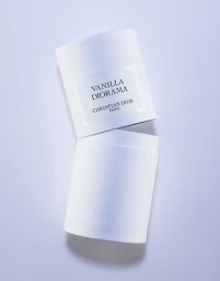 White cylinder perfume box angled open against a pale blue background, photographed by Coppi Barbieri