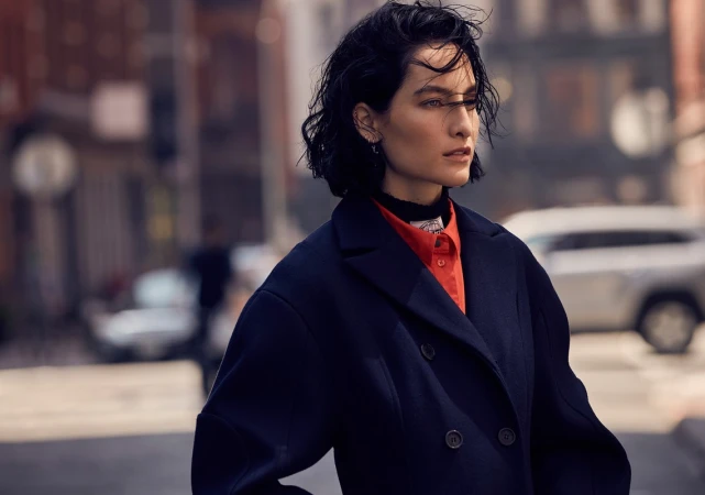 A woman with dark wet-look hair wearing a navy coat and red shirt on a city street in Los Angeles.