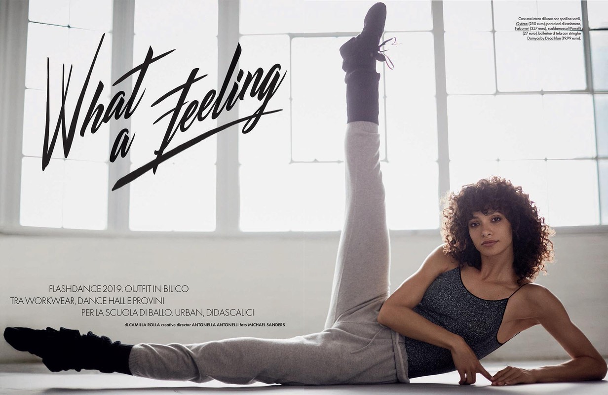 Adult woman with curly hair in athletic wear, lying on the floor with legs raised and against a studio background. Lifestyle, fashion editorial.