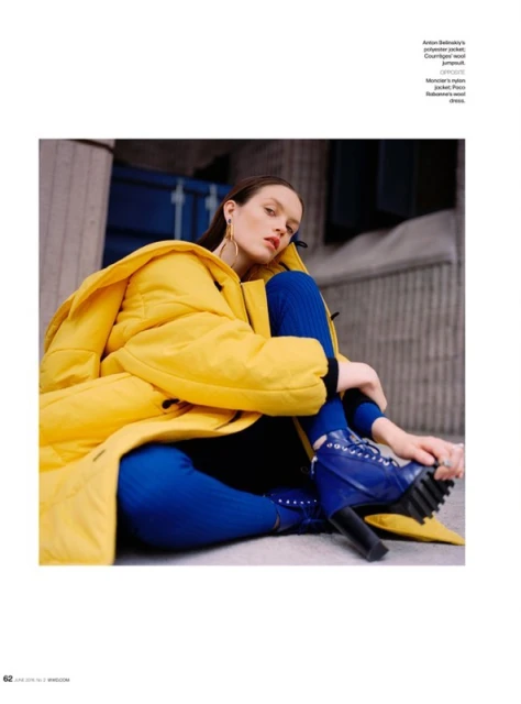 A young woman in a yellow puffer jacket and blue knit pants sits on a concrete structure looking at the camera in an editorial fashion shot.