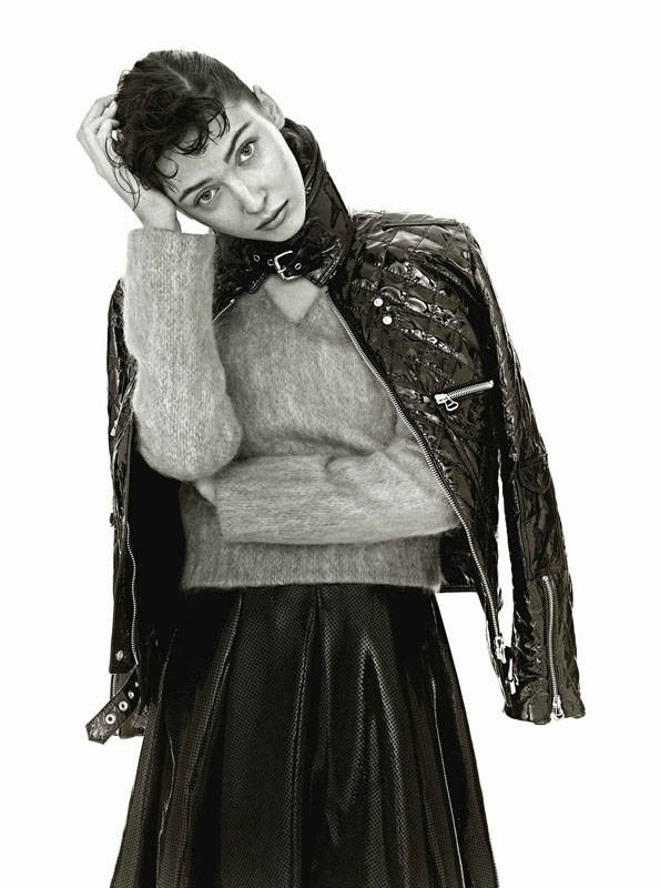 Monochrome fashion portrait of adult female in a black patent leather jacket and skirt, posing in a studio with a neutral expression.