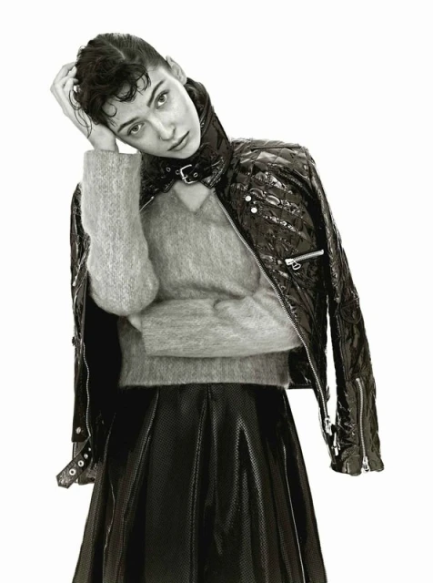 Monochrome fashion portrait of adult female in a black patent leather jacket and skirt, posing in a studio with a neutral expression.