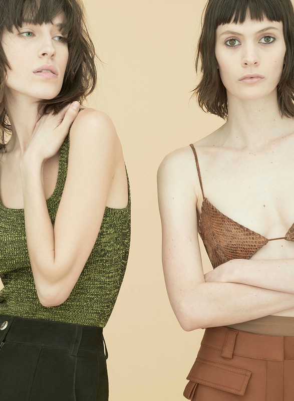 Two adult women pose indoors against a solid background, wearing fashionable tops and high-waisted trousers in a studio shot.