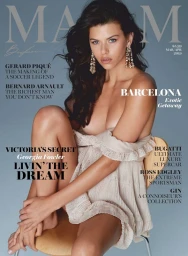 Magazine cover portrait of a woman with dark hair seated on a wooden stool against a muted grey background.