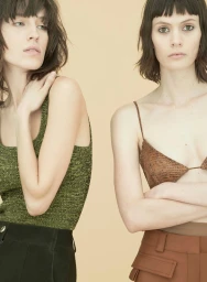 Two female models with dark hair and bangs posing against a plain backdrop, featuring make-up artistry by Cynthia Sobek.