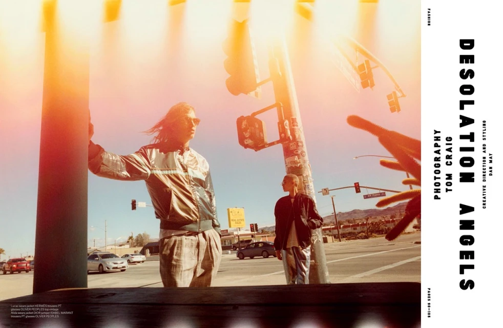 Fashion editorial shot of two adults posing on a street corner with traffic lights, cars, mountains and buildings in the background.