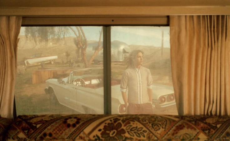 Scene from inside a motor home featuring a convertible and a person standing outside on a bright day with a desert background.