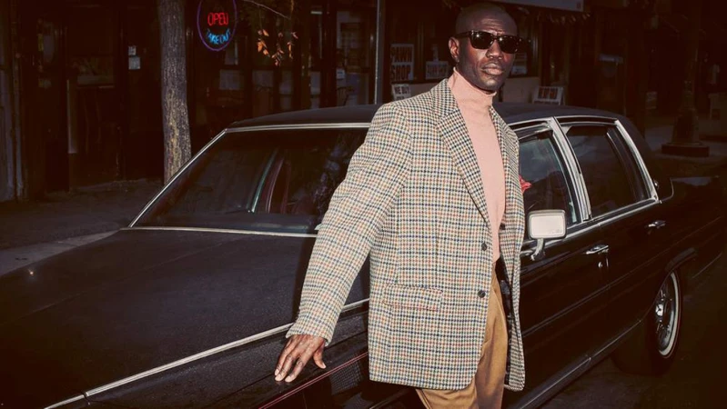 Black man wearing houndstooth blazer and sunglasses leaning on a vintage car in Los Angeles