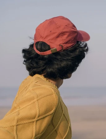 Person wearing a red baseball cap and mustard yellow knit sweater outdoors, viewed from behind.