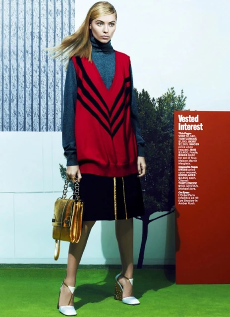 Fashion editorial image featuring a blonde model wearing a red sweater vest, black skirt, metallic handbag, and white heels outdoors.