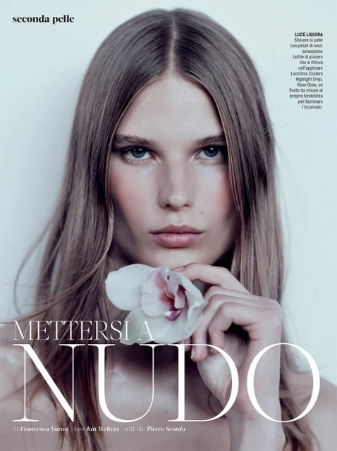 Beauty shot of a young adult woman with long blonde hair holding a white orchid flower, studio lighting, fashion editorial.