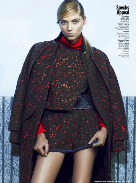 Fashion editorial shot of a woman in a patterned co-ord set and coat with a red turtleneck, posing in front of a textured wall.