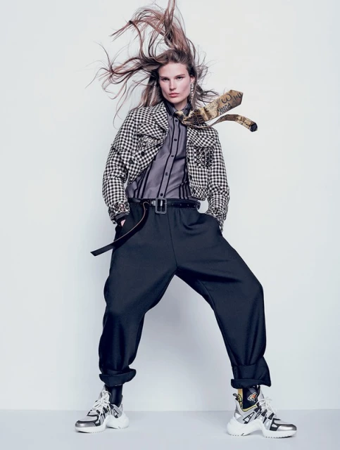 Fashion editorial shot of a female model with long hair, wearing a black and white checkered jacket, black pants and silver chunky sneakers.