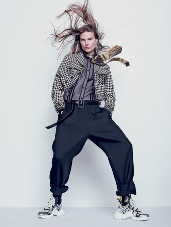 Fashion editorial shot of a female model with long hair, wearing a black and white checkered jacket, black pants and silver chunky sneakers.