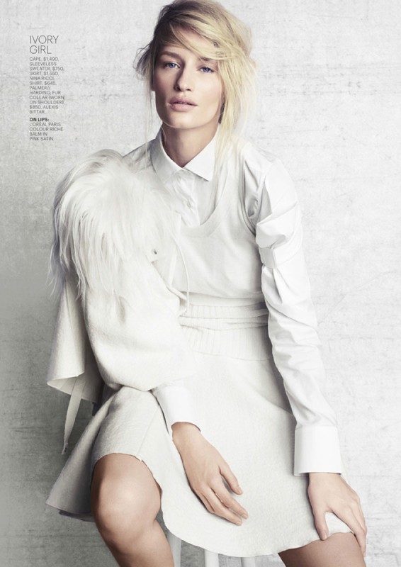 Elegant woman in white outfit poses in front of textured gray wall, fashion portrait for Visie, editorial style.