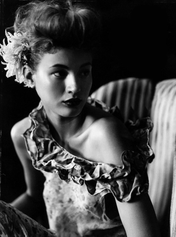 Elegant black and white portrait of a young woman with an updo hairstyle adorned with flowers and wearing a ruffled dress.