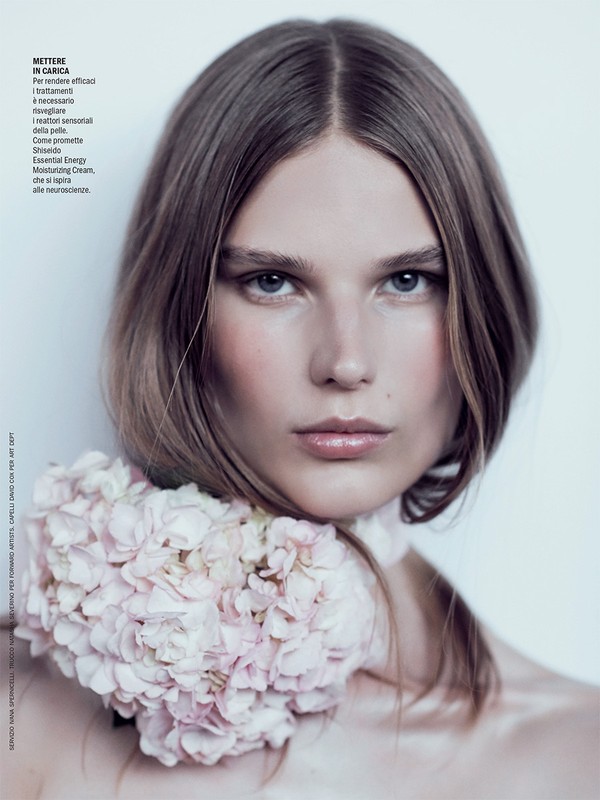 Close-up portrait of a woman with center-parted brown hair wearing a pink floral collar against a pale background