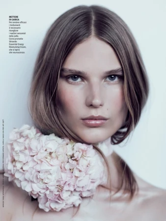Close-up portrait of a woman with center-parted brown hair wearing a pink floral collar against a pale background