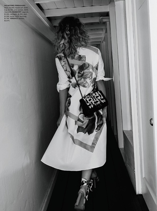 A woman is walking down a hallway wearing a floral print dress, black and white heels, and a beaded black purse over her shoulder.