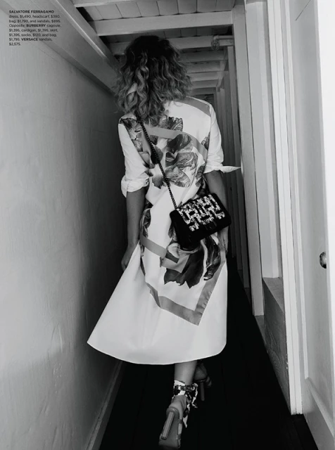 A woman is walking down a hallway wearing a floral print dress, black and white heels, and a beaded black purse over her shoulder.