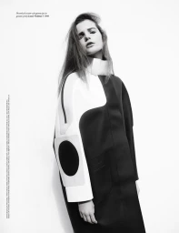 Black and white portrait of a female model wearing a structured color-block coat with high collar against a white backdrop.