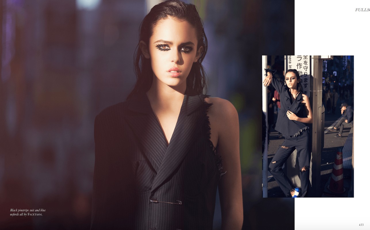 Fashion editorial shot of a young woman with heavy eye makeup wearing a pinstripe jacket in an urban setting with an edgy, street-style look.