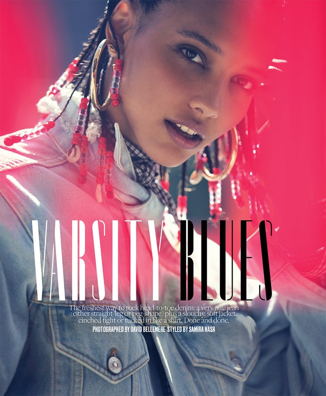 Close-up portrait of a woman wearing a denim jacket, large gold hoop earrings with red beads, and braided hair.