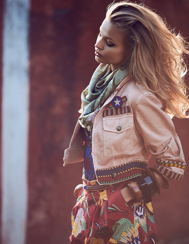 Fashion shot of a blonde woman in a stylish, light jacket and floral skirt, posing against a blurred background with soft, diffused lighting.