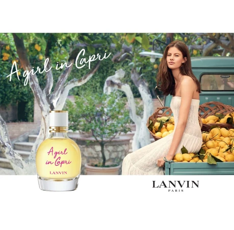 Woman sits on a teal truck bed surrounded by lemons next to a bottle of A Girl in Capri perfume in an outdoor garden setting.