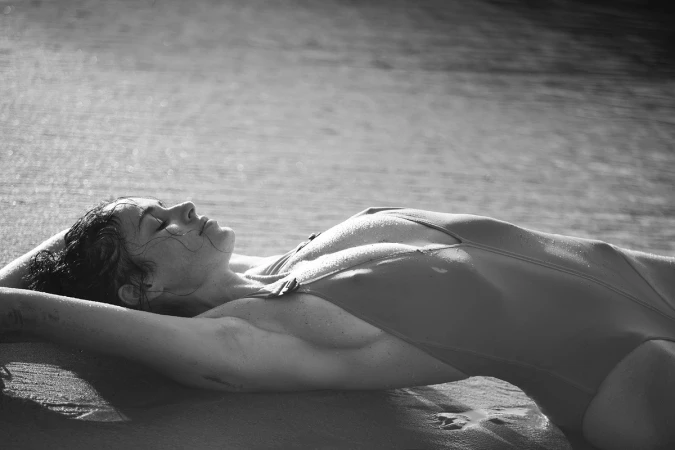 Monochrome portrait of a woman lying on a sandy beach wearing a one-piece swimsuit, photographed by David Bellemere.