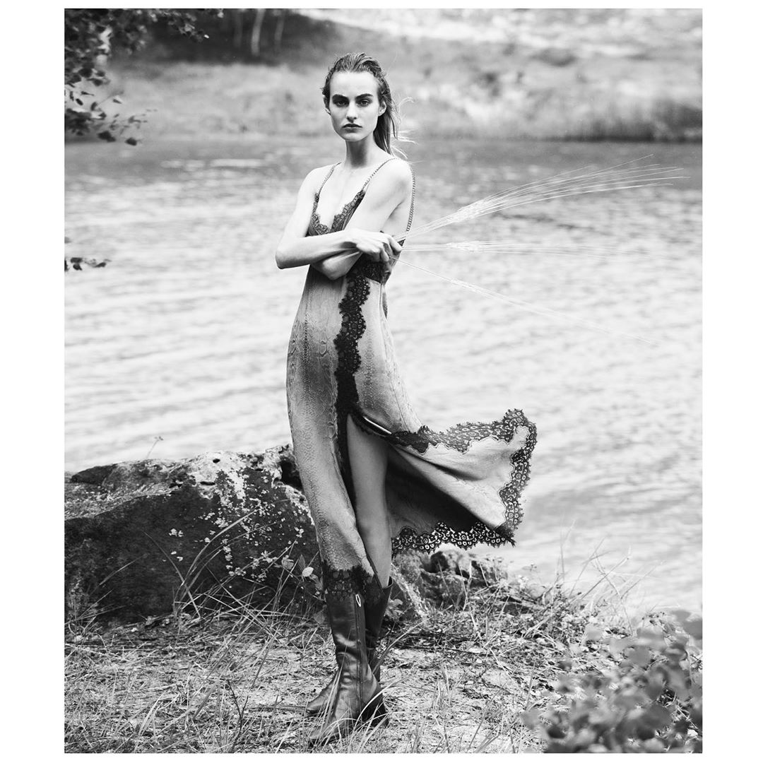 Model in a lace-trimmed dress and knee-high boots standing by a lake, photographed by David Bellemere