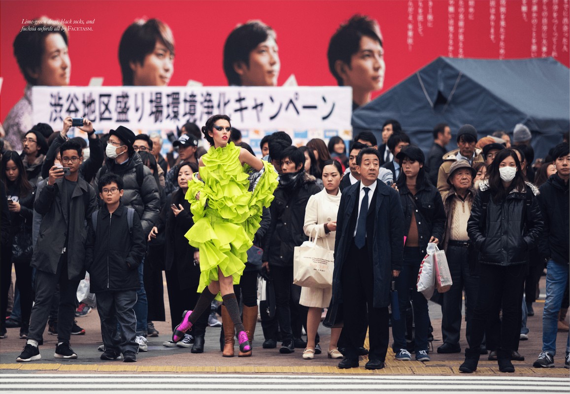 Model in vibrant lime green ruffled dress walking through a crowded city street with onlookers