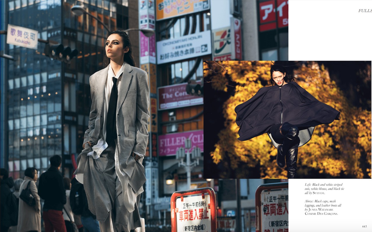 Editorial fashion shot: Woman in oversized grey suit poses in Tokyo street, buildings and pedestrians blurred in background. Runway look.