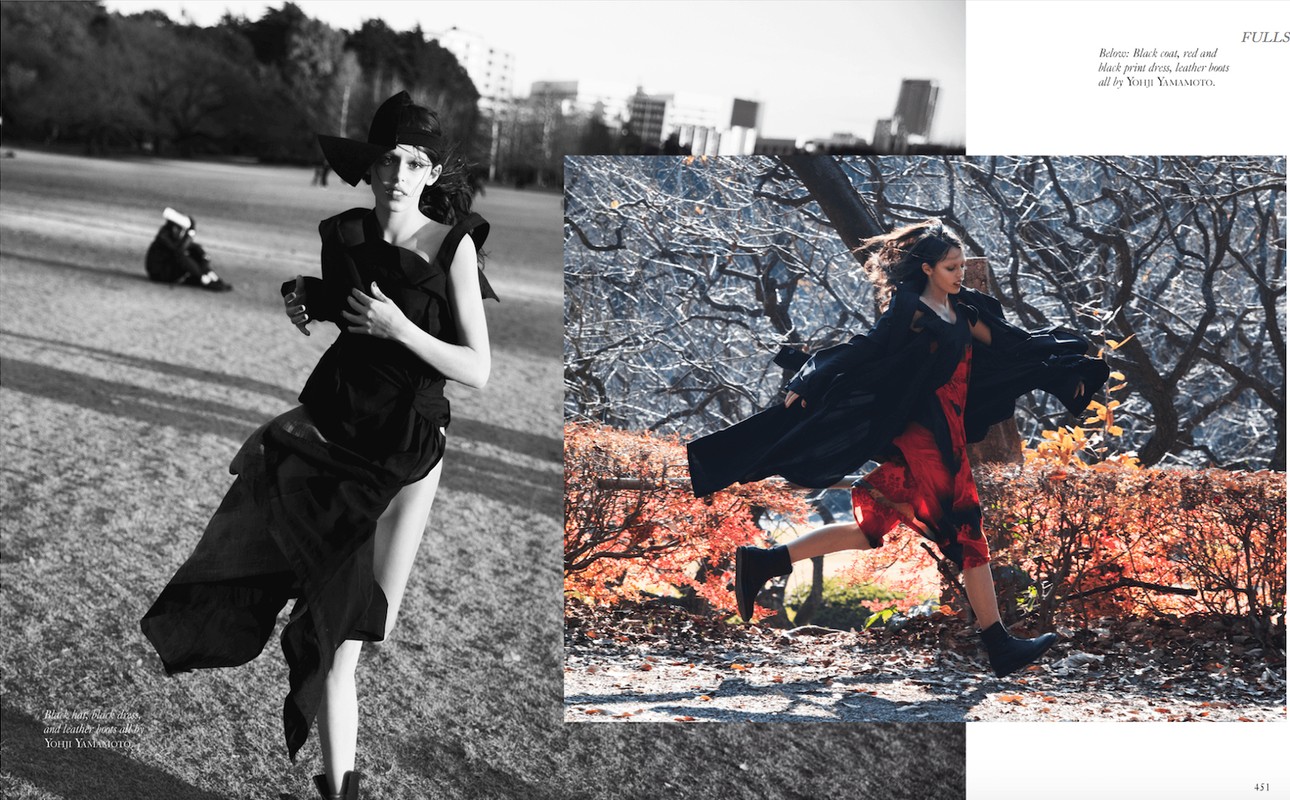 Black and white fashion editorial shot of a woman in avant-garde black clothing running in a grassy field with cityscape background.