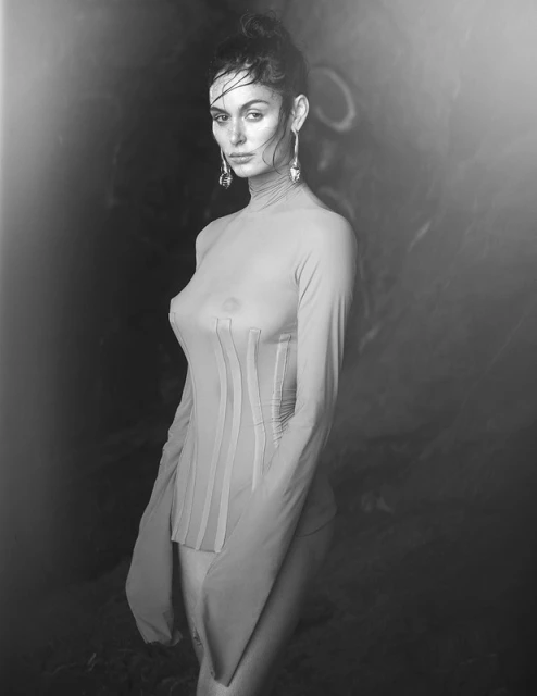 Monochrome portrait of a woman with an elegant updo wearing a long-sleeved top with embellishments, posing against a blurred background.