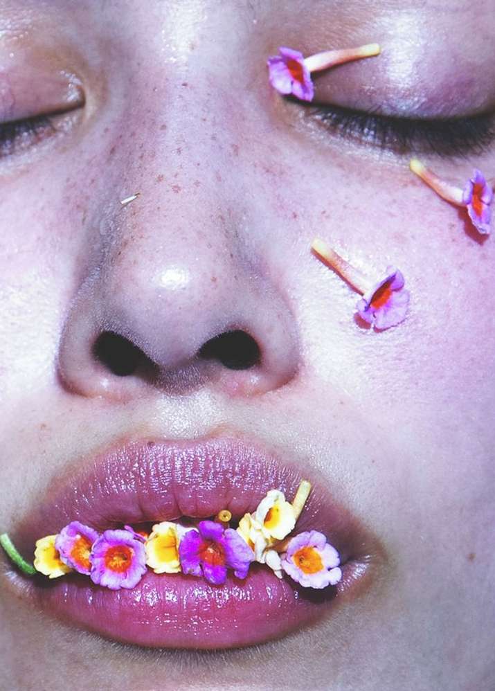 Close-up of a person's face with eyes closed and flowers on their lips and eyelids in a beauty or wellness concept image.