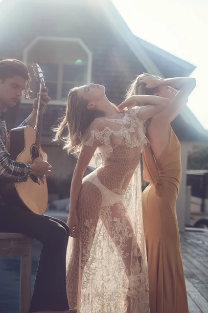 Outdoor fashion shot featuring a male guitarist and two female models in dresses, one wearing a white lace dress, in natural lighting.