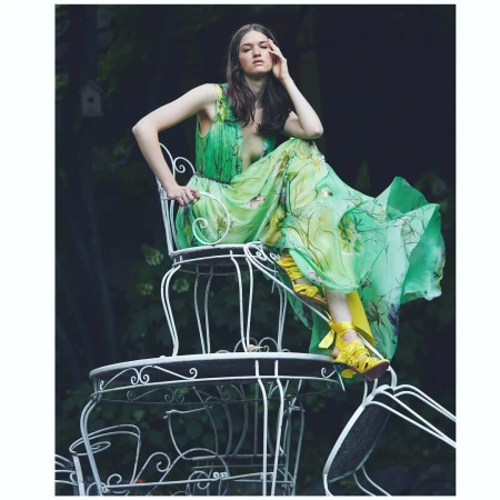 Woman in a green floral dress seated on stacked white iron chairs outdoors