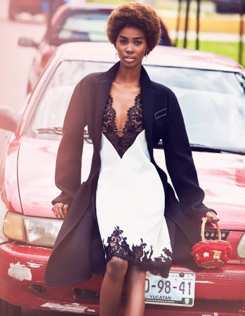Black woman with an afro wearing a black coat and a white dress with black lace leaning against a red car