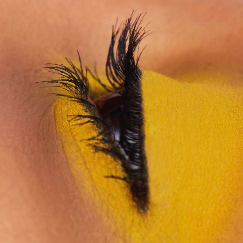 Close-up shot of a woman's eye with black eyelashes and bold yellow eyeshadow on her eyelid and under her eye for beauty.