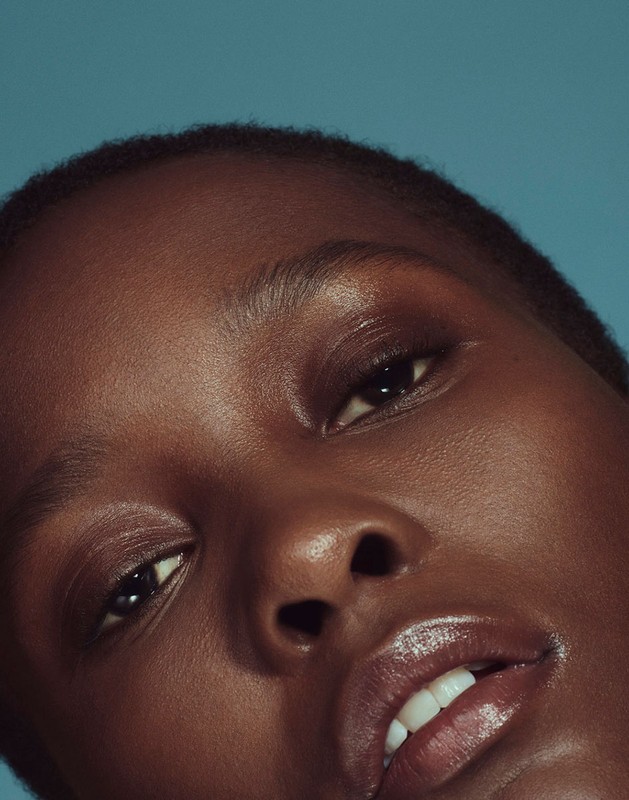 Close-up shot of a young Black woman's face with a glowing complexion against a solid turquoise background. Beauty, skin, cosmetics.