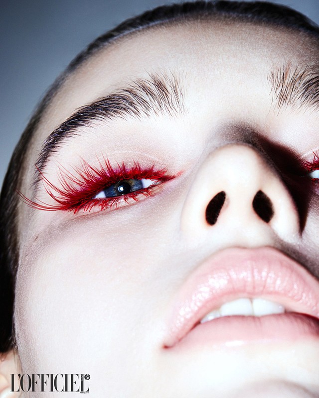 Close-up of a young adult female face looking up. Red false eyelashes, pink lips, and clear skin are featured in a studio fashion beauty shot.
