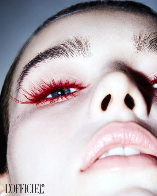Close-up of a young adult female face looking up. Red false eyelashes, pink lips, and clear skin are featured in a studio fashion beauty shot.