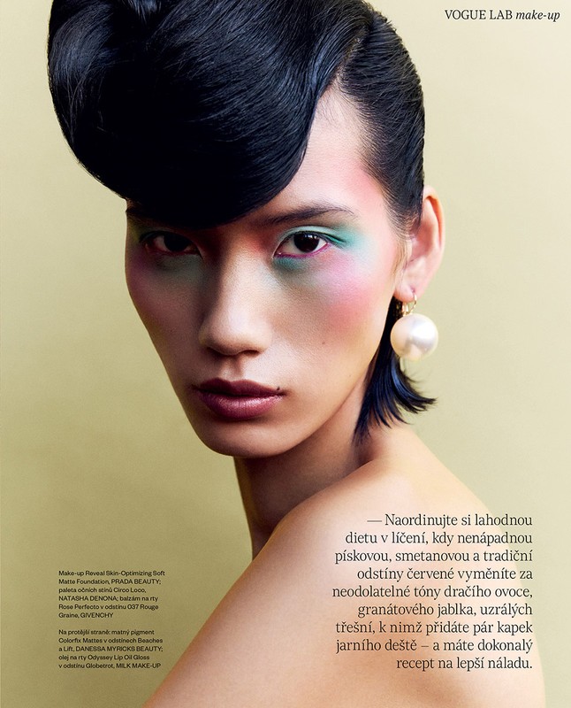 Close-up portrait of a model with sculpted black hair, vibrant eye makeup, and a large pearl earring.