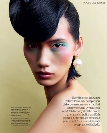 Close-up portrait of a model with sculpted black hair, vibrant eye makeup, and a large pearl earring.