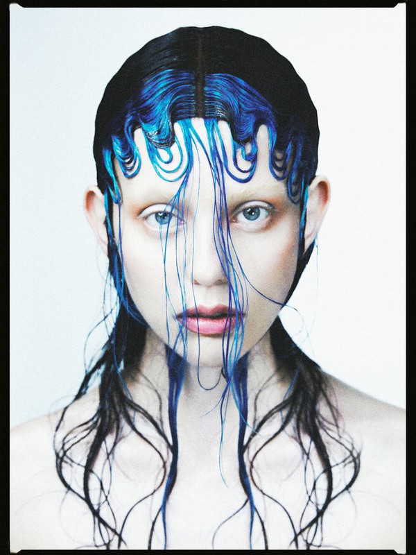 Striking close-up of a fashion model with creative black and blue hair, showcasing edgy beauty and avant-garde style in a studio setting.