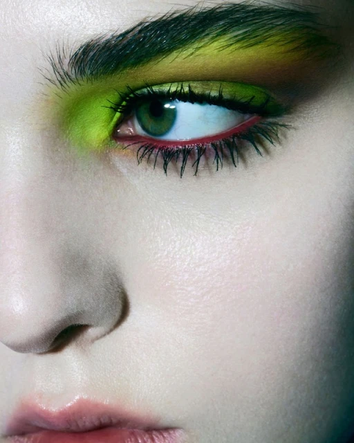 Close-up of a woman's face with green eyeshadow, striking red eyeliner, and full lashes in a beauty or cosmetic context.