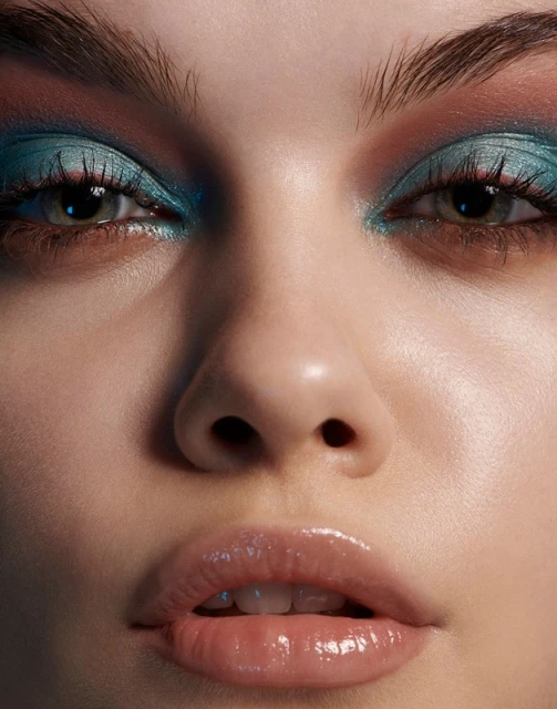 Close-up portrait of a fair-skinned woman with blue eyeshadow, visible glossy lips, and soft studio lighting, showcasing beauty.