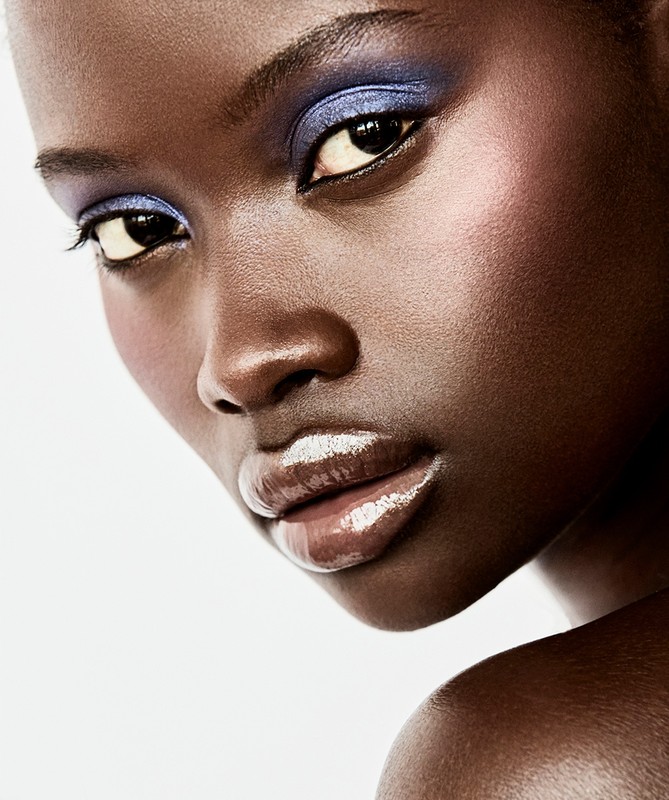 Close-up beauty portrait of an African American woman with brown skin and glossy lips, showcasing vibrant blue eyeshadow makeup.