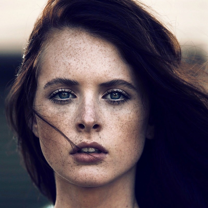 Close-up portrait of a woman with freckles and dark hair framing her face by makeup artist David Razzano